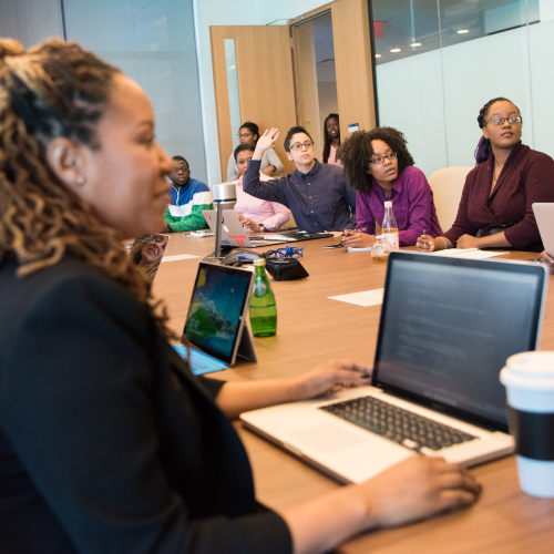 A group of diverse coworkers sit at a conference table and talk.