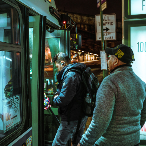 Two white men board a public bus in the evening.