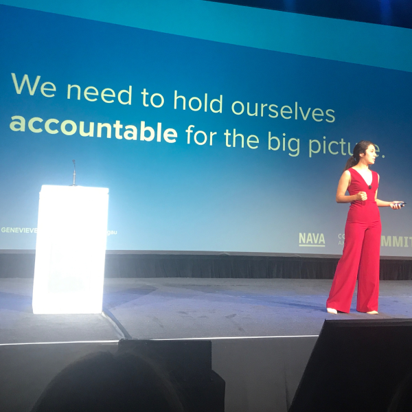 A white woman and Nava employee presents on a stage in front of a screen that says "We need to hold ourselves accountable for the big picture."