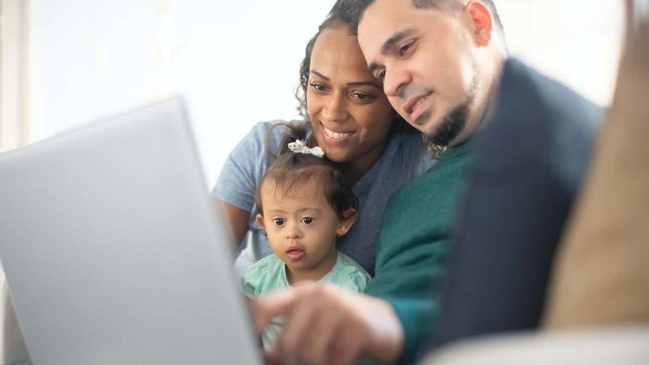 A Black woman and a Latino man hold their baby and look at a computer. 