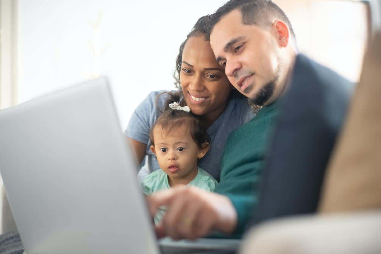 A Black woman and a Latino man hold their baby and look at a computer. 