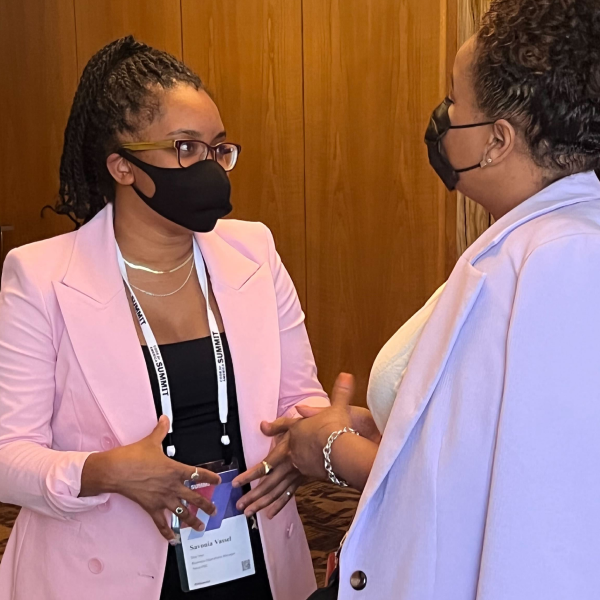Two Black women, one of whom is a Nava employee, chat while wearing face masks at a conference.