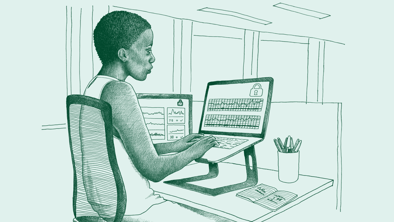 A middle-aged Black woman sits at a desk working on a computer. Her screen shows secure data information. 
