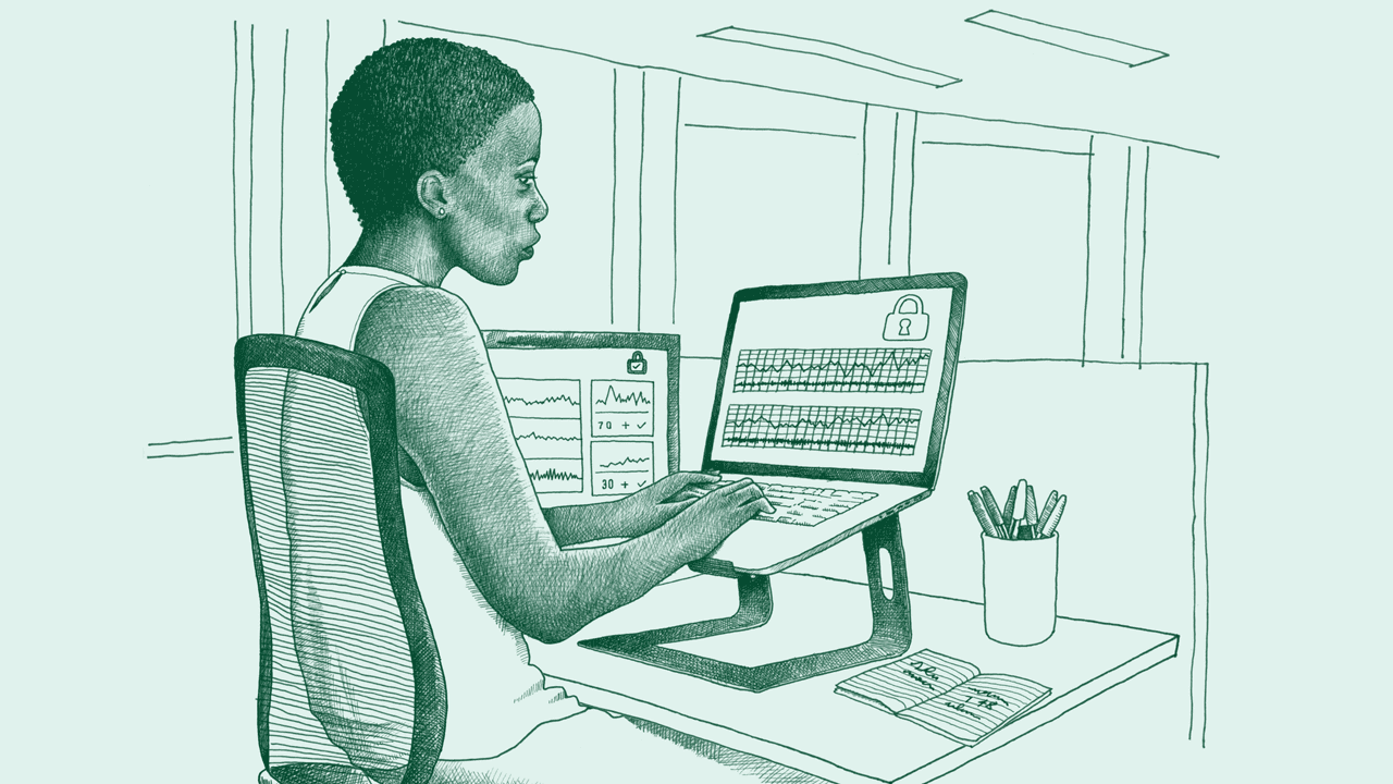 A middle-aged Black woman sits at a desk working on a computer. Her screen shows secure data information.