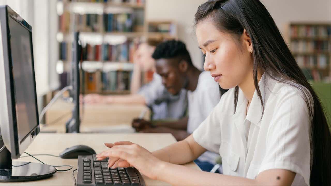 An Asian woman works at a computer in a library.