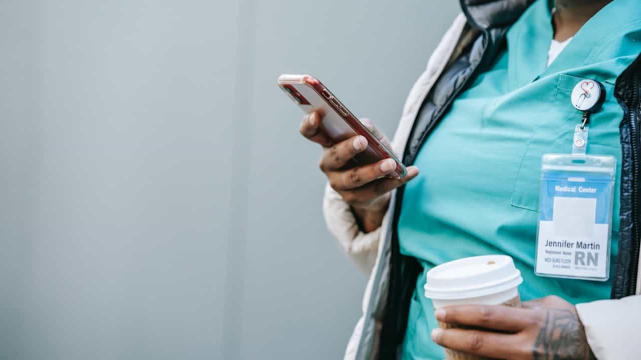 A Black healthcare worker in scrubs uses an iphone.
