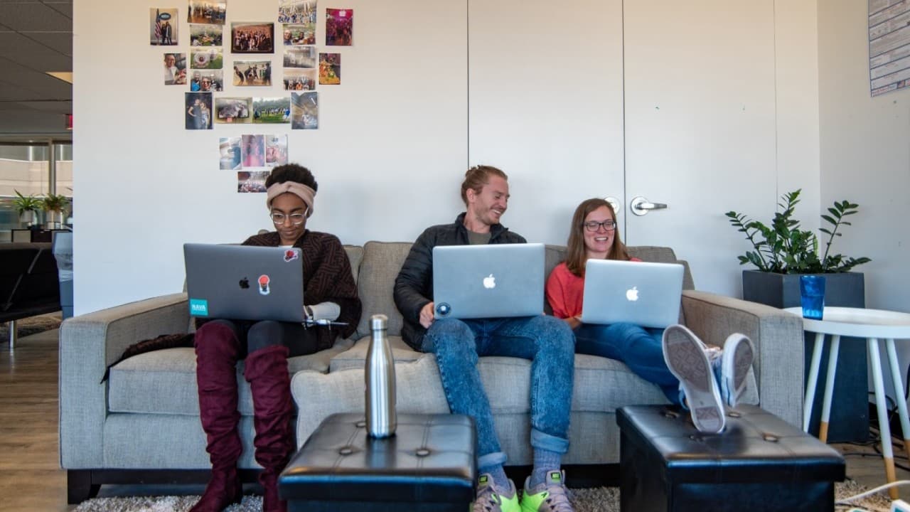 Alsia Plybeah sitting on a couch in the Washington, D.C. office working on a laptop.