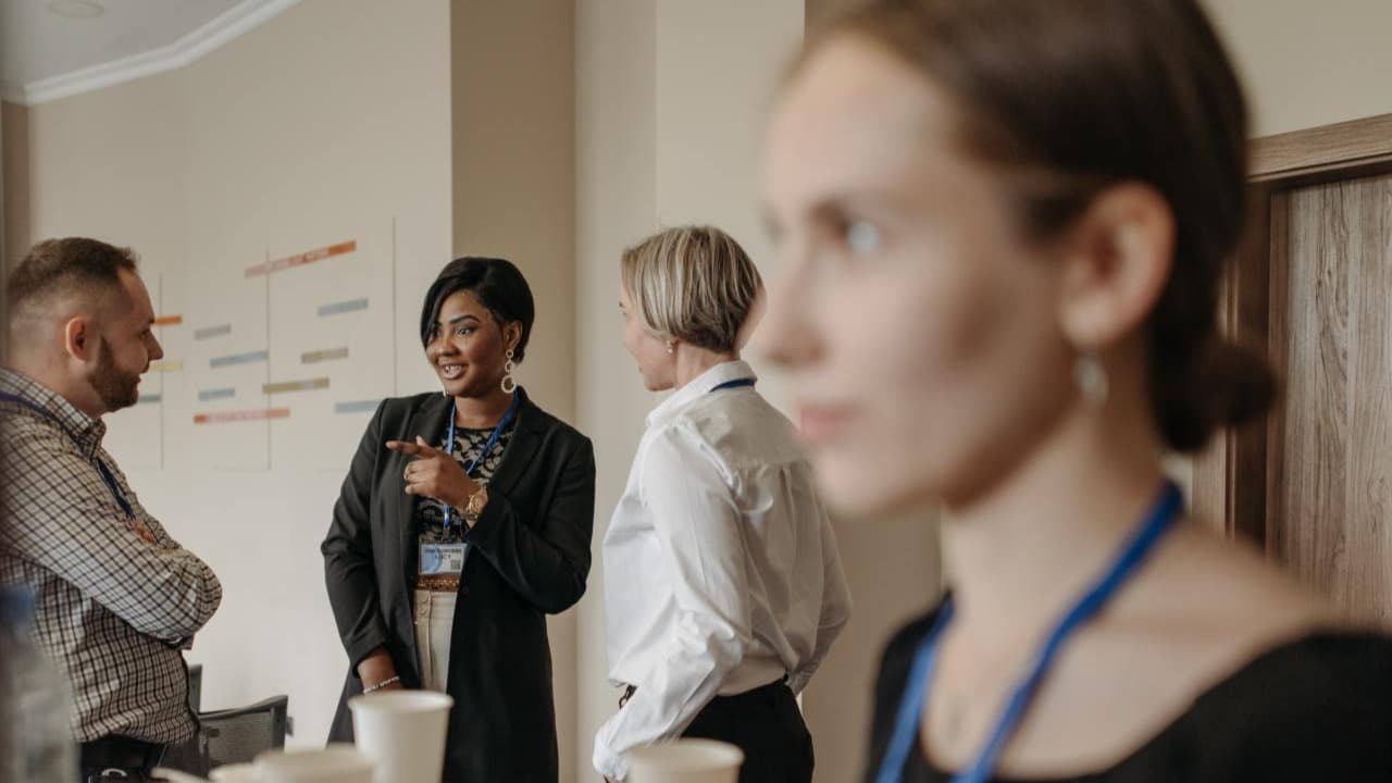 A diverse group of office workers stand and talk during a lunch break in a meeting room.
