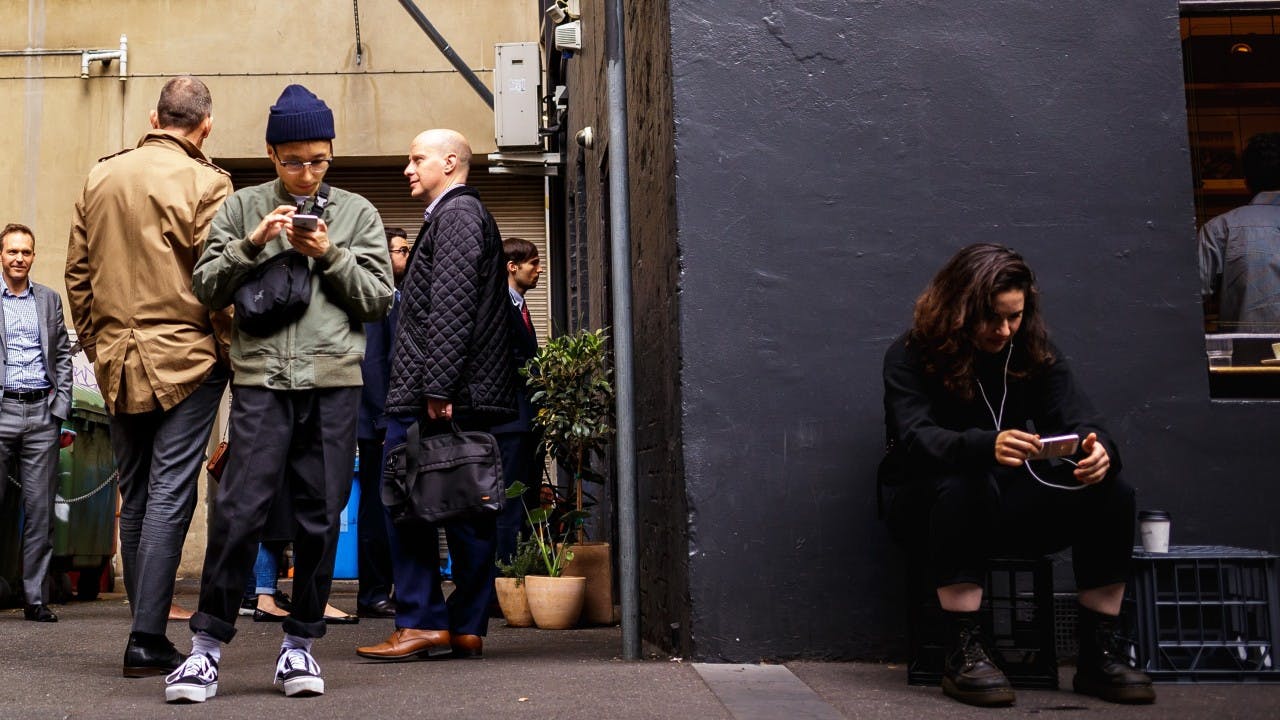 A group of diverse people use their phones while standing in line.