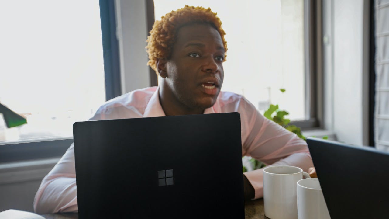 A Black man sits behind a laptop. 