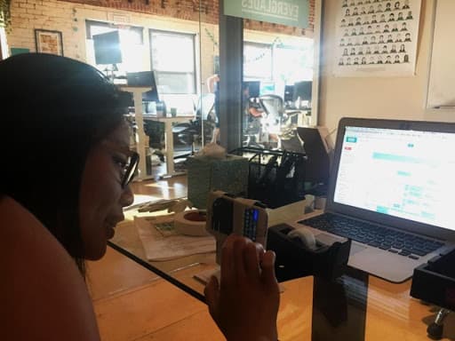 A photo of an Asian woman using a smartphone that's attached to a stand in front of a laptop computer screen.