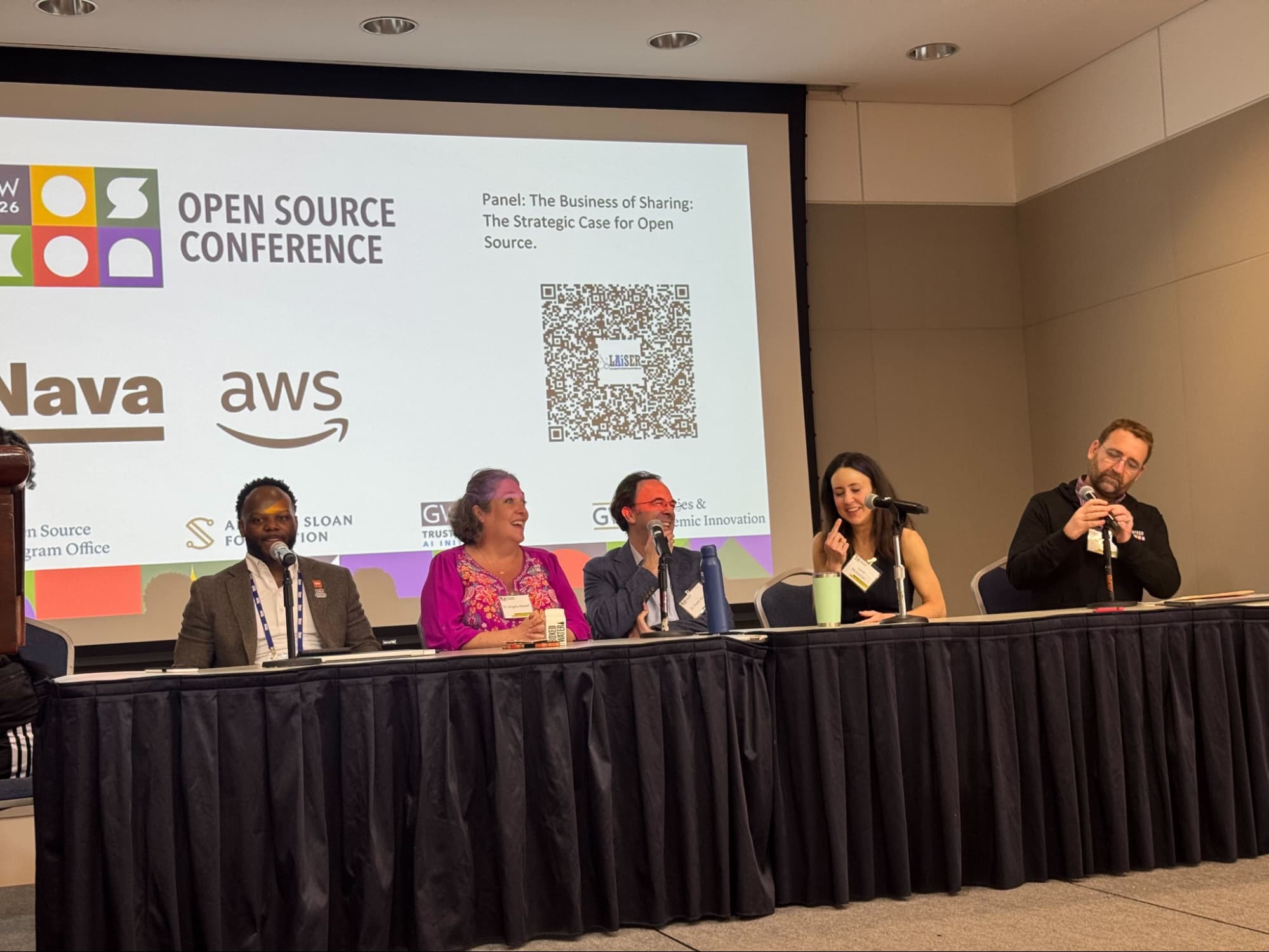 Five panelists sit at a table in front of a screen.