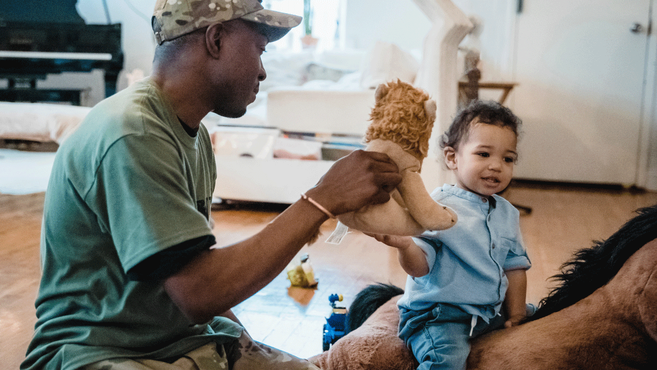 A Black Veteran plays with his baby using a stuffed tiger.