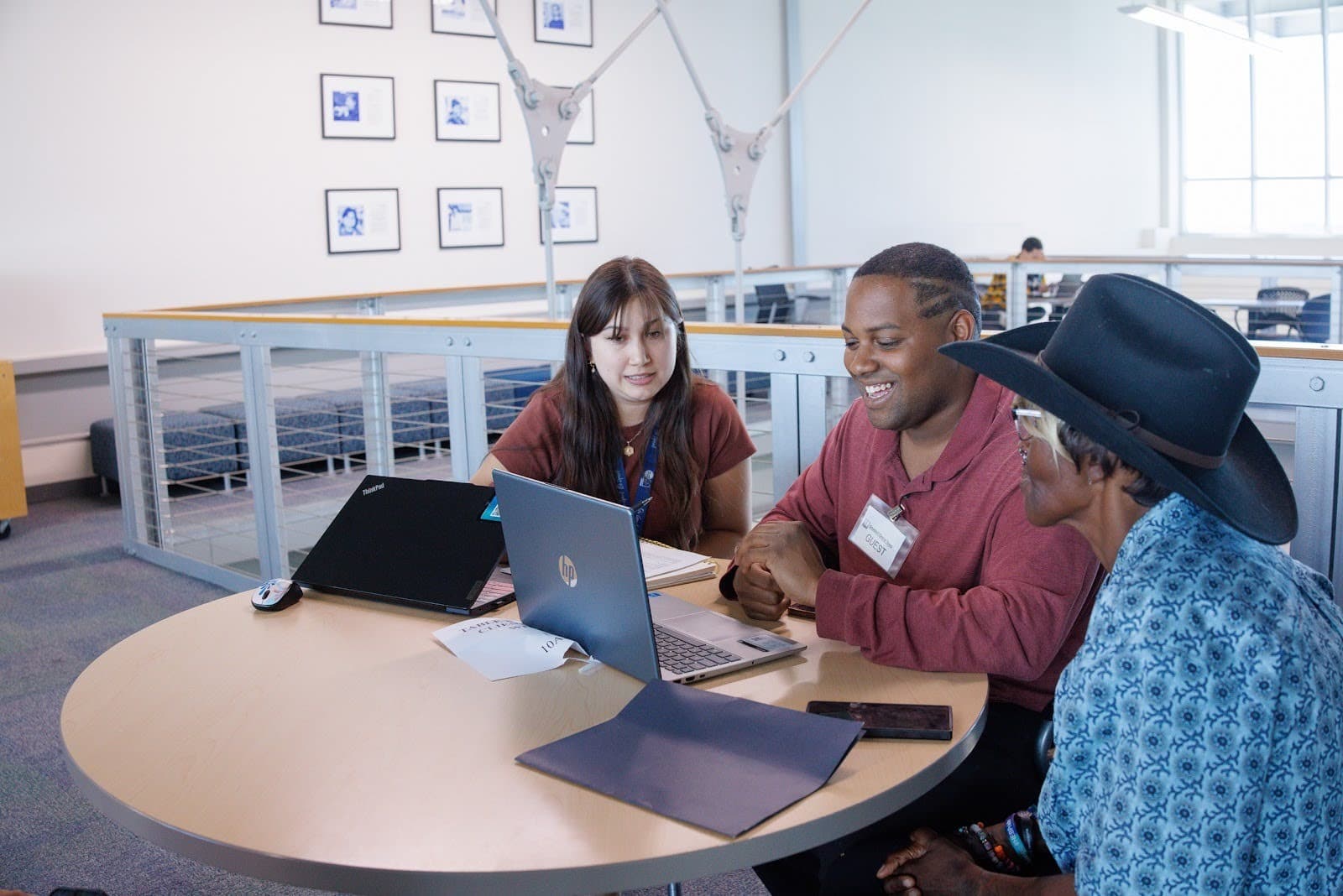 Three adults sit at a round table, using a laptop together to review information and discuss results.