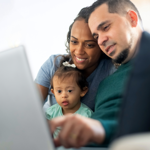 A Black mother, father, and their baby look at laptop together.