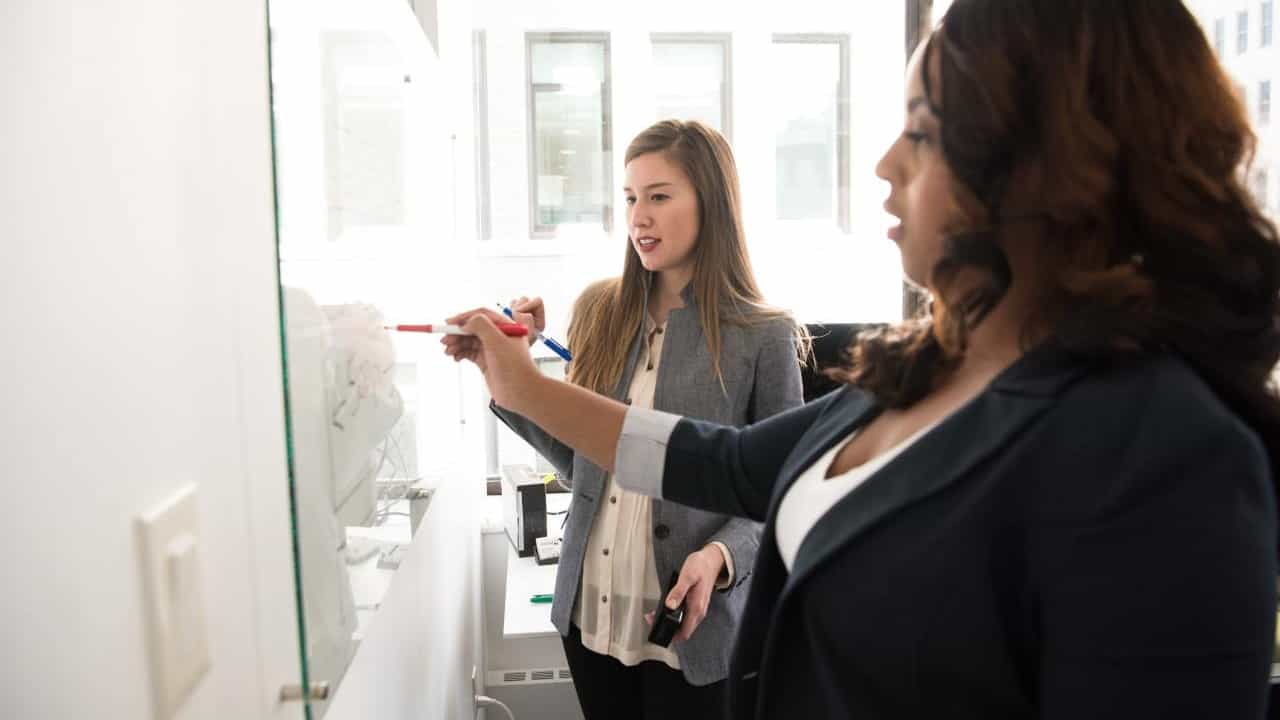 Two women work at a whiteboard.